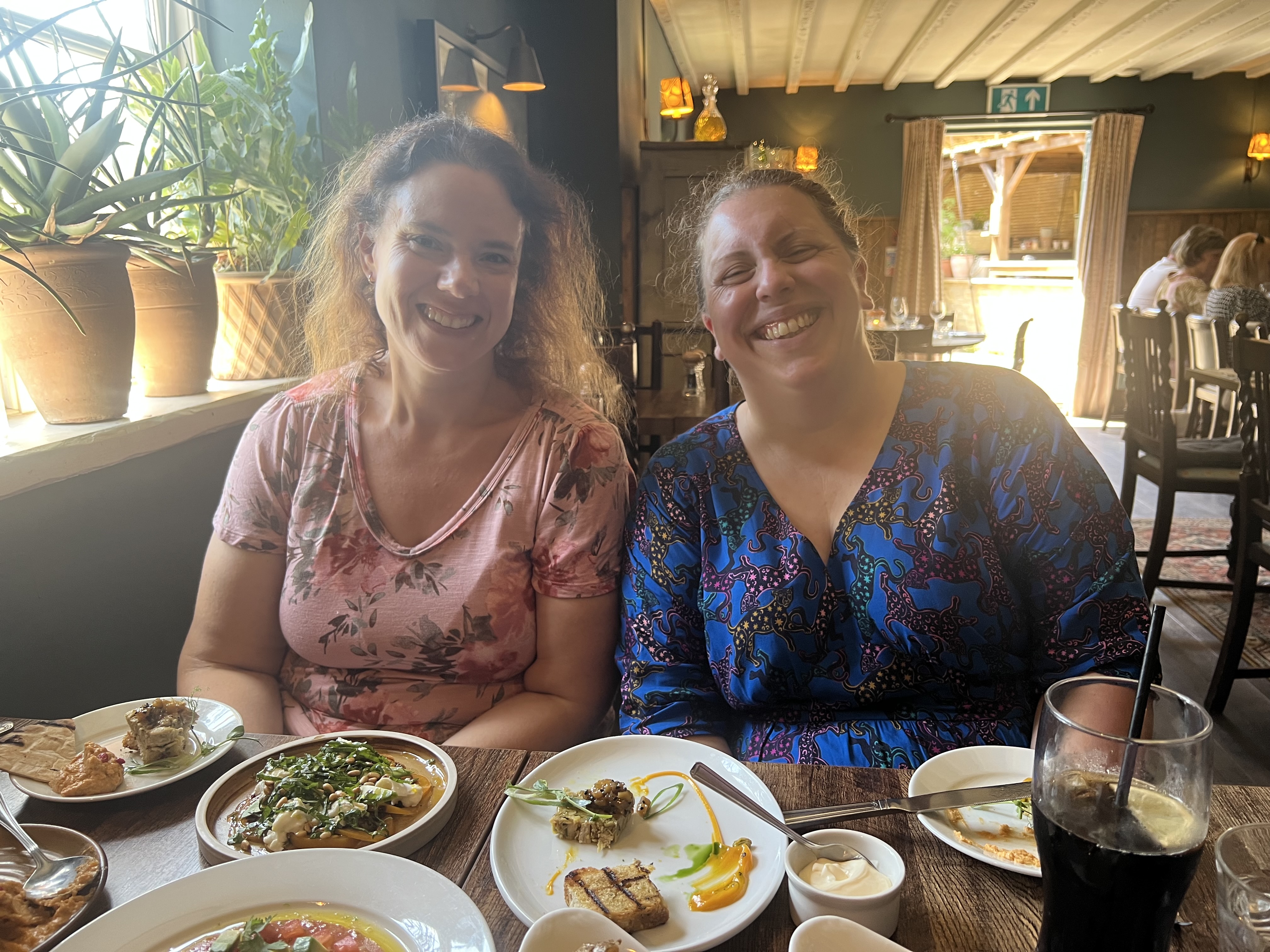 Lise and Jen smiling at the table covered with plates of food at the Lamb Inn in Crawley